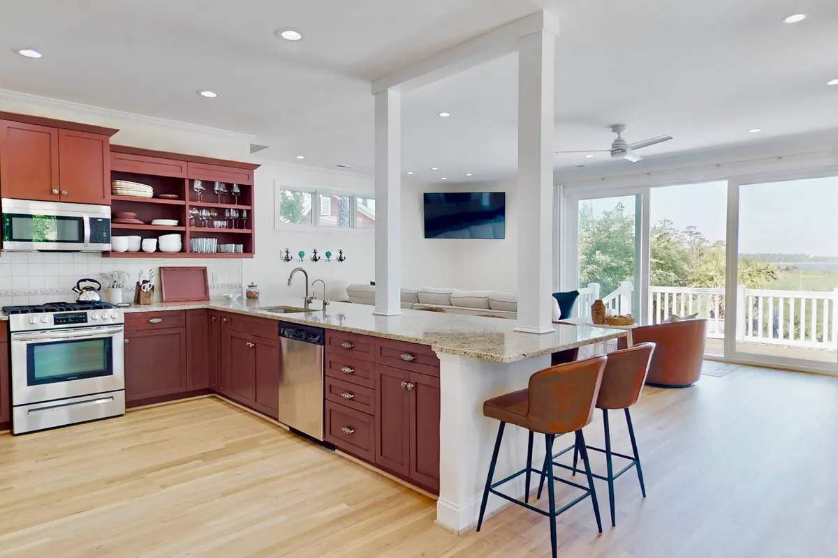 A vibrant kitchen scene with a red-accented island, large windows framing nature views, and ample space for cooking and entertaining. Bar stools line the island, making it ideal for group meal prep or casual dining.