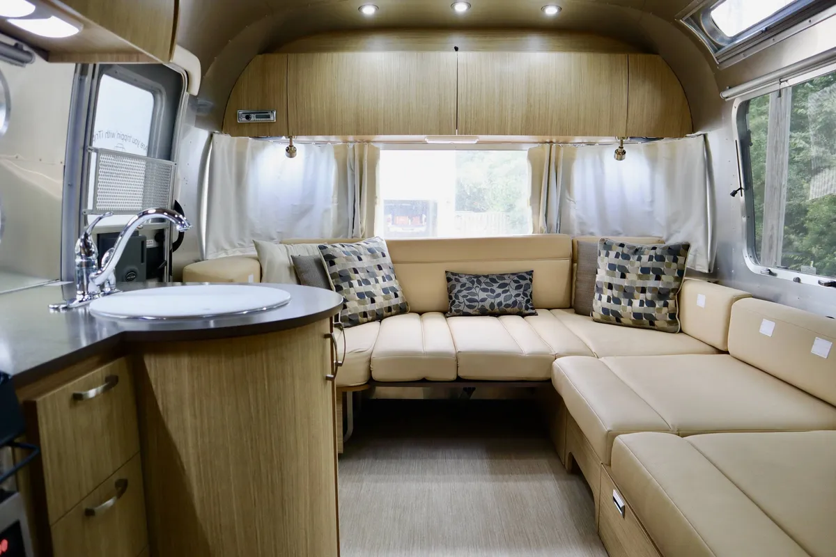 An interior shot of the Airstream guest suite, featuring a curved seating area with patterned cushions and a modern kitchenette. The cozy and inviting design illustrates the comfort and self-contained nature of the suite, supporting features such as electricity and private amenities.