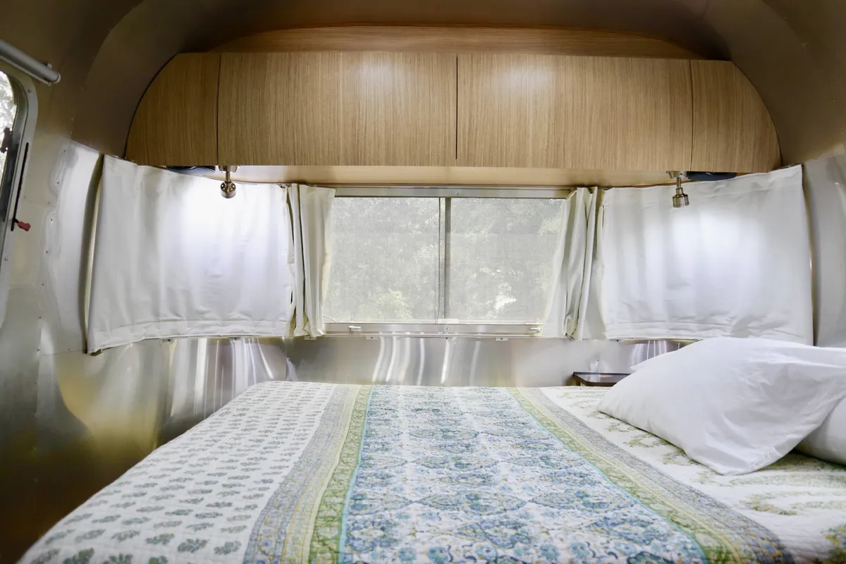 A tranquil interior photo of the Airstream’s queen bed with patterned bedding and a large window, surrounded by wooden cabinetry. Natural light streams in, emphasizing the serene and private retreat guests can enjoy.