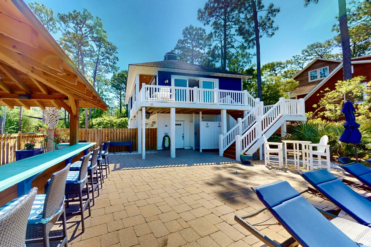 A lively outdoor entertaining space featuring a swimming pool area, an outdoor bar, and a deck with comfortable seating. The area is bathed in cheerful light and designed for gatherings, dining, and poolside fun with friends.