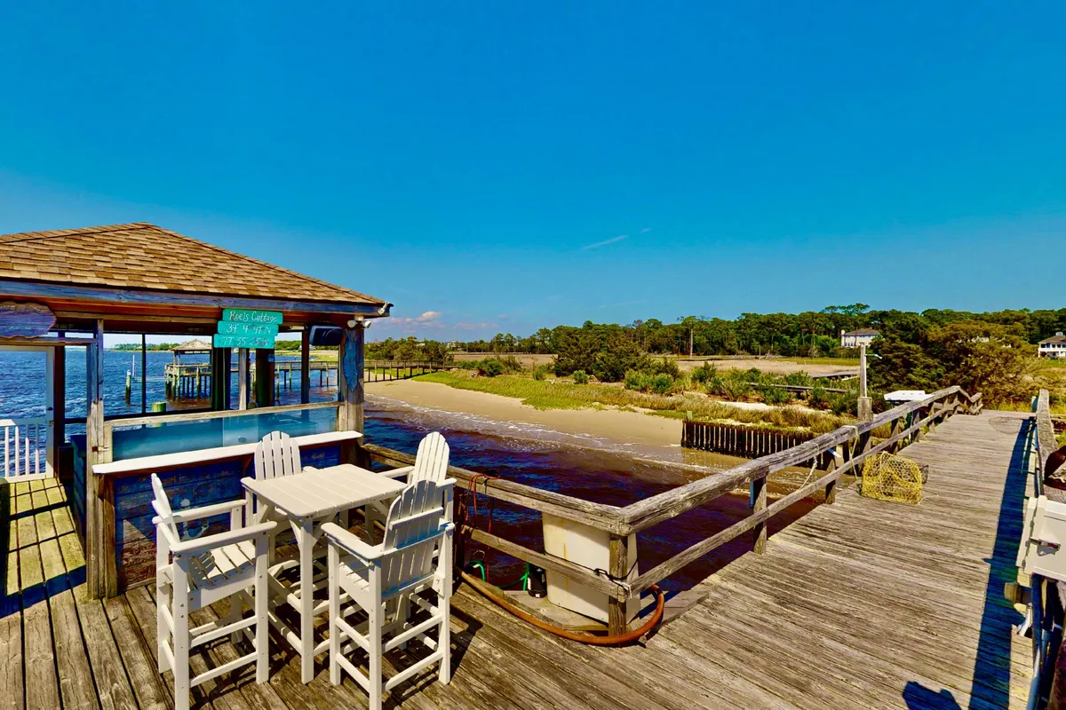 A serene waterfront scene featuring a comfortable outdoor seating area set beside a gently flowing river. A pier structure extends over the water, providing ample space for relaxed walks and opportunities for fishing. The natural surroundings are lush and green, inviting guests and their pets to enjoy the open air and scenic views.