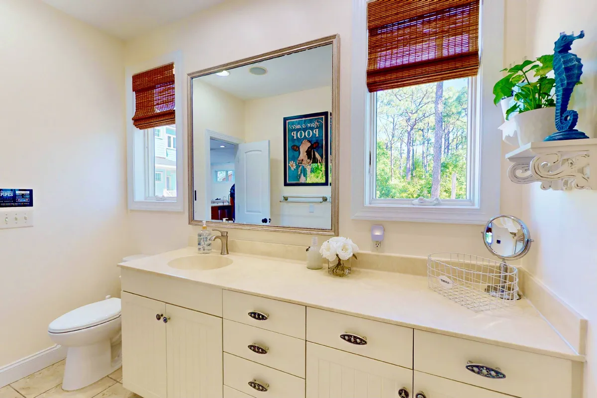 A modern, organized bathroom with a large mirror, stylish sink area, and subtle décor touches like a decorative plant and wall art. The space feels bright, clean, and inviting—perfect for self-care routines and ensuring privacy and convenience for guests in both sleeping areas.
