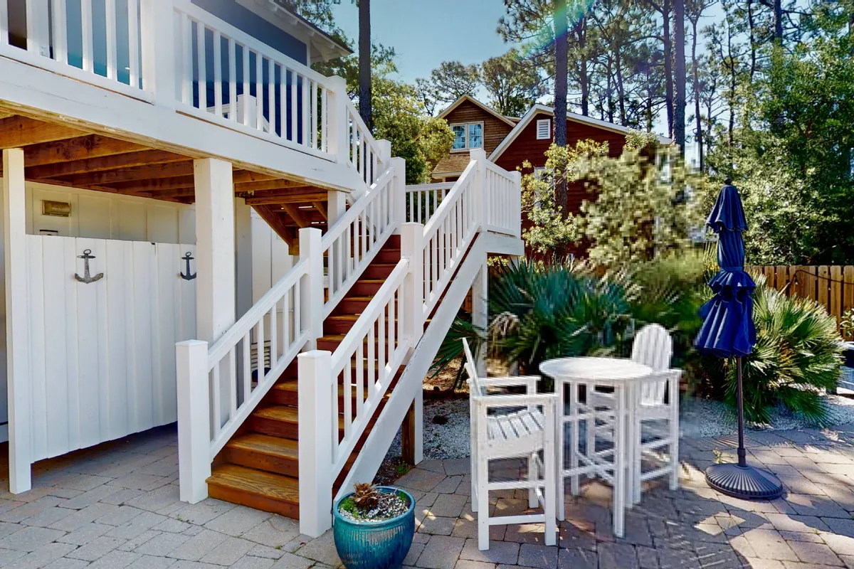 A casual exterior scene with a staircase leading to an outdoor seating arrangement, including a potted plant and umbrella. The setup offers a relaxed, social atmosphere in a well-maintained environment, ideal for enjoying meals, reading, or gathering with friends.