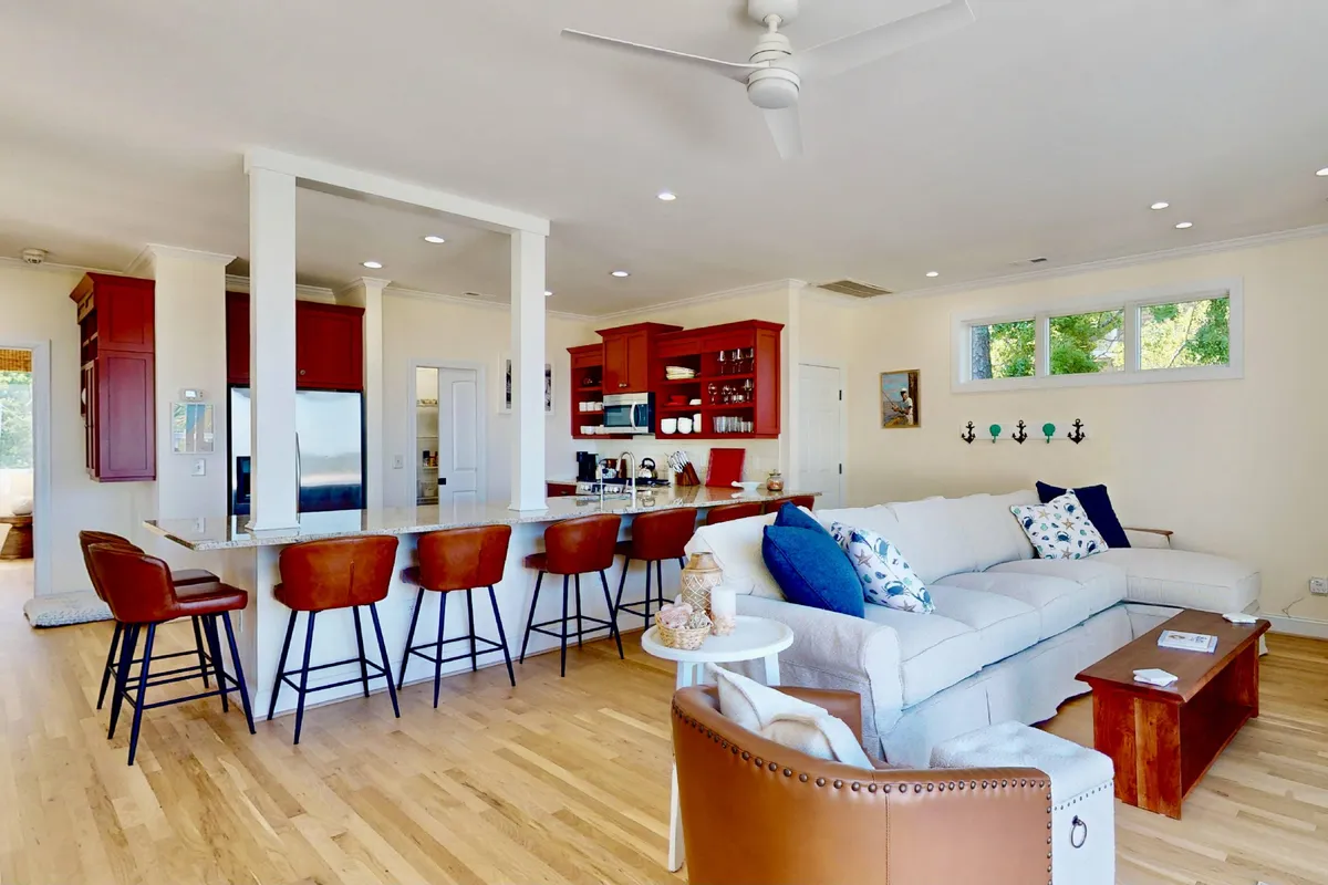 An inviting open-plan room that combines the kitchen and living area. The kitchen features a prominent island with bar stools, while the living room offers a comfortable sofa. The spaces are bright and spacious, perfect for both cooking and relaxing.