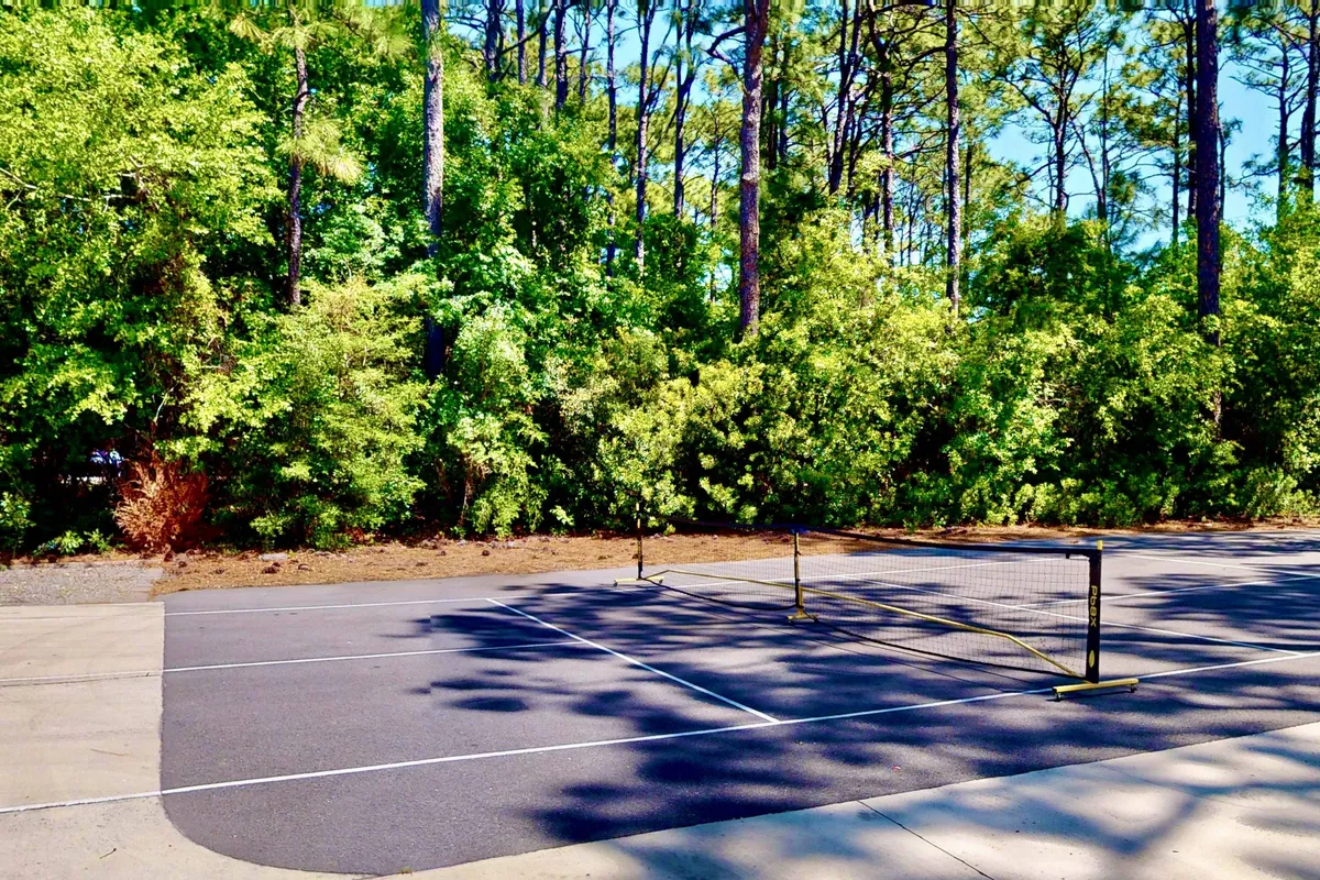 A well-maintained tennis court surrounded by lush greenery, with a net ready for play. The court's placement in a tranquil outdoor setting hints at recreational fun and invites friendly competition among guests.