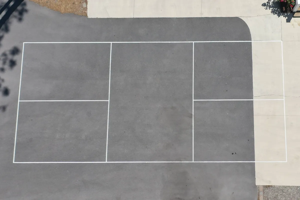 An asphalt court marked for pickleball and other games, ready for friendly matches and active outdoor fun. The court is surrounded by open air and greenery, emphasizing a lively, recreational atmosphere.