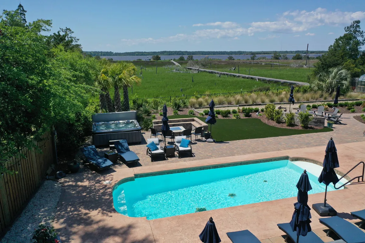 A spacious swimming pool surrounded by lounge chairs and tall palm trees, with an outdoor dining area nearby. The pool sits in a landscaped area overlooking the natural scenery, suggesting easy access from the main house and inviting family fun under the sun.