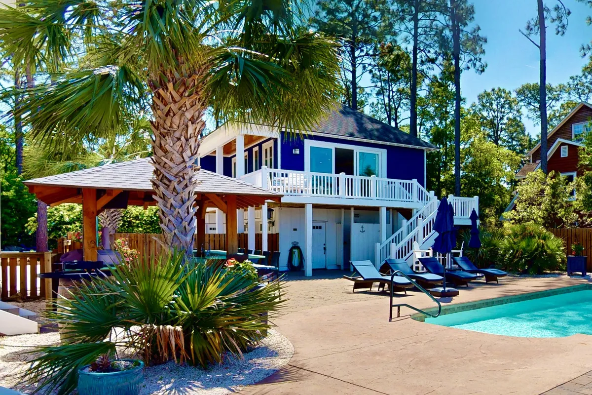 The image highlights a sparkling swimming pool flanked by palm trees and a spacious deck area, set against the home's exterior. It creates a cheerful and luxurious mood, emphasizing fun outdoor activities like swimming, sunbathing, and dining al fresco.